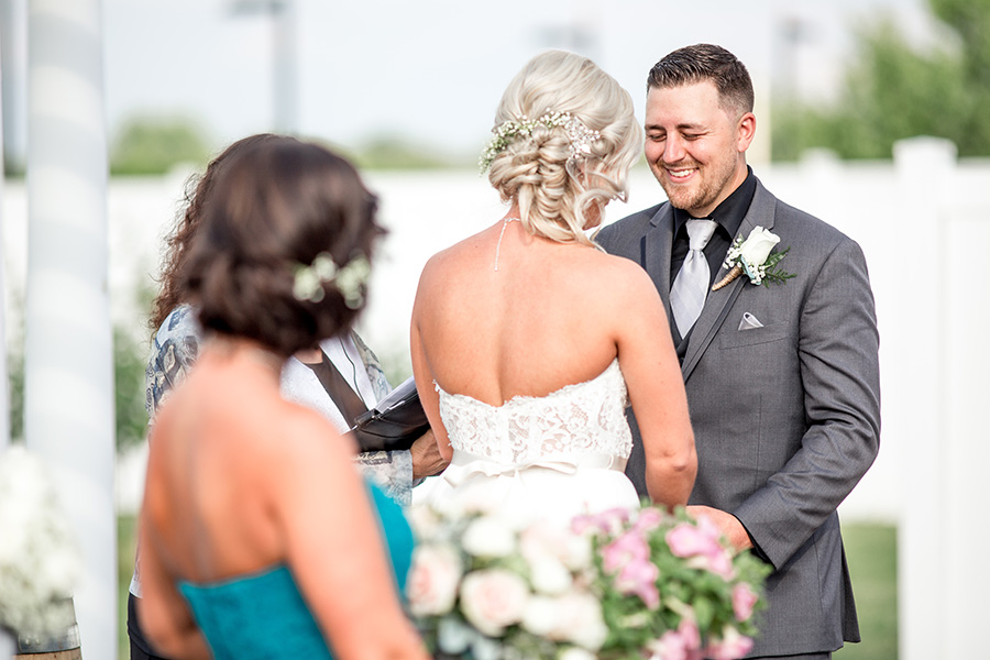 groom smiles at his bride during the wedding ceremony at tomasello winery