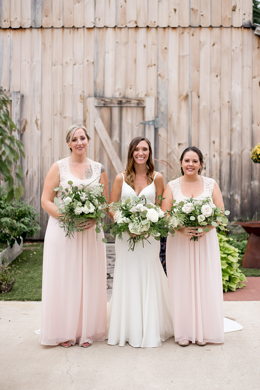 bride and bridesmaids pose with the neutral background in front of the barn