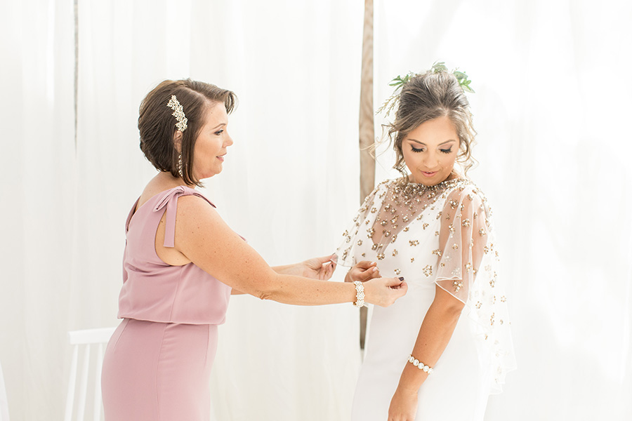 Mom helps bride into dress in the greenhouse at Bast Brothers