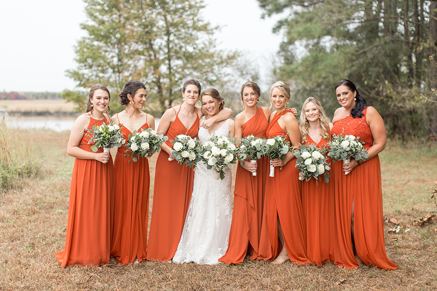 Bridesmaids in burnt orange floor-length dresses with white bouquets